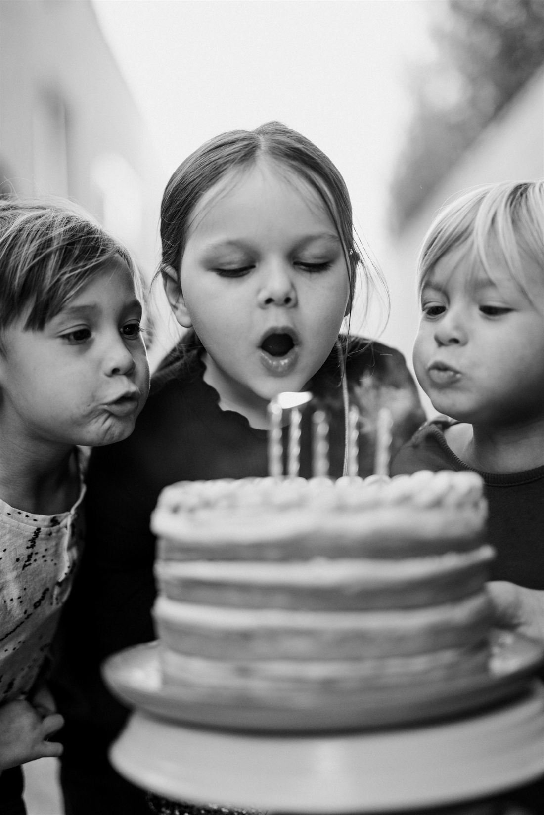 Drei Kinder pusten gemeinsam die Kerzen einer Geburtstagstorte aus, Schwarz-Weiß