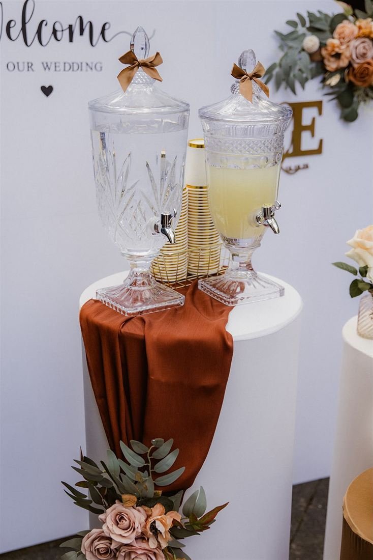 Getränkestation mit Glaskaraffen und Rosen vor einer Hochzeitswand